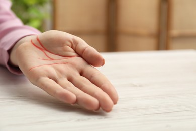 Chiromancy and foretelling. Woman showing palm with drawn lines at white wooden table, closeup. Space for text