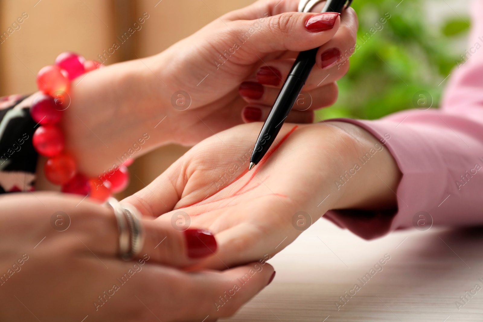 Photo of Fortune teller reading lines on woman's palm at white wooden table, closeup. Chiromancy