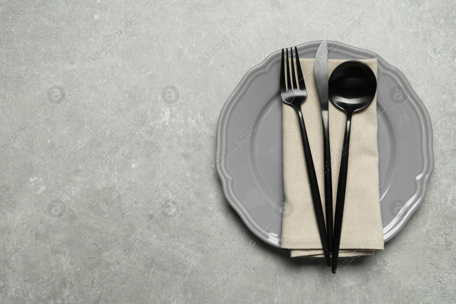 Photo of Stylish cutlery, napkin and plate on grey table, top view. Space for text