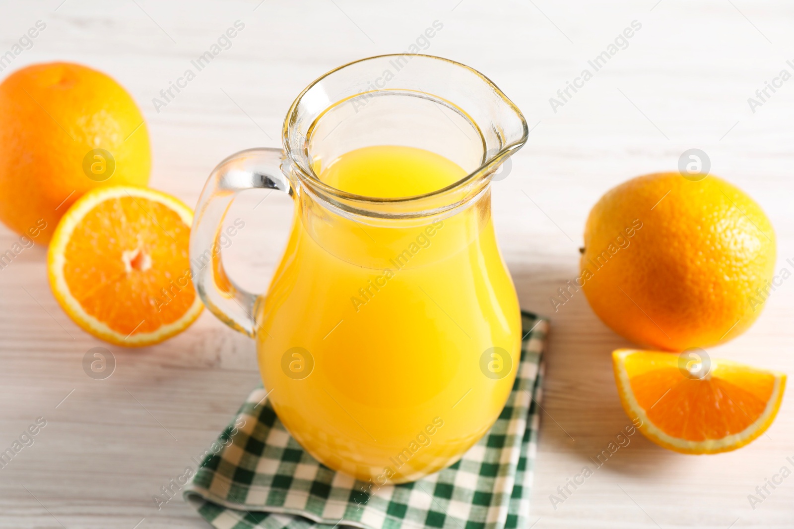 Photo of Tasty orange juice in glass jug and fresh fruits on white wooden table