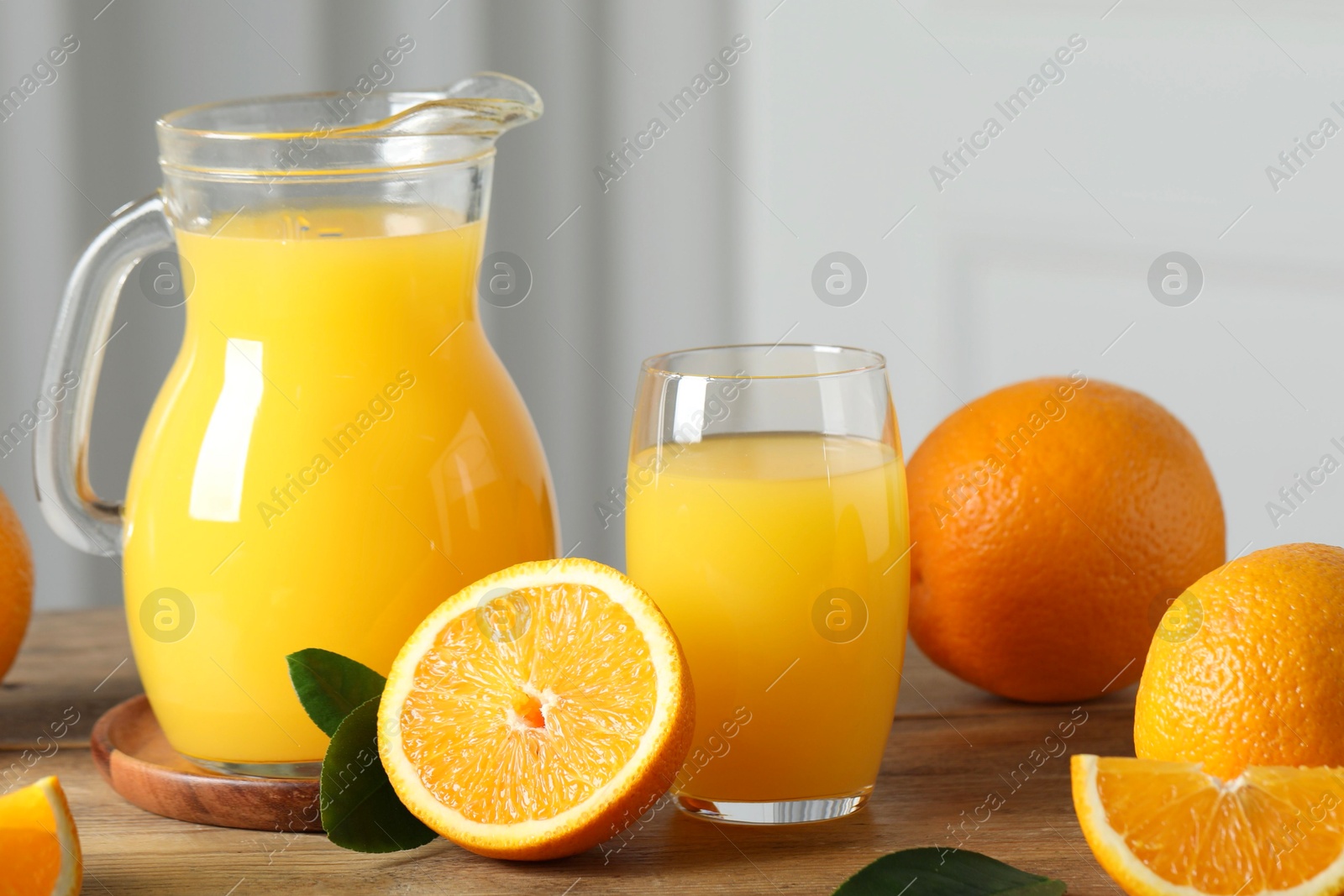 Photo of Tasty orange juice, green leaves and fresh fruits on wooden table