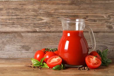 Tasty tomato juice in glass jug, fresh vegetables and spices on wooden table. Space for text