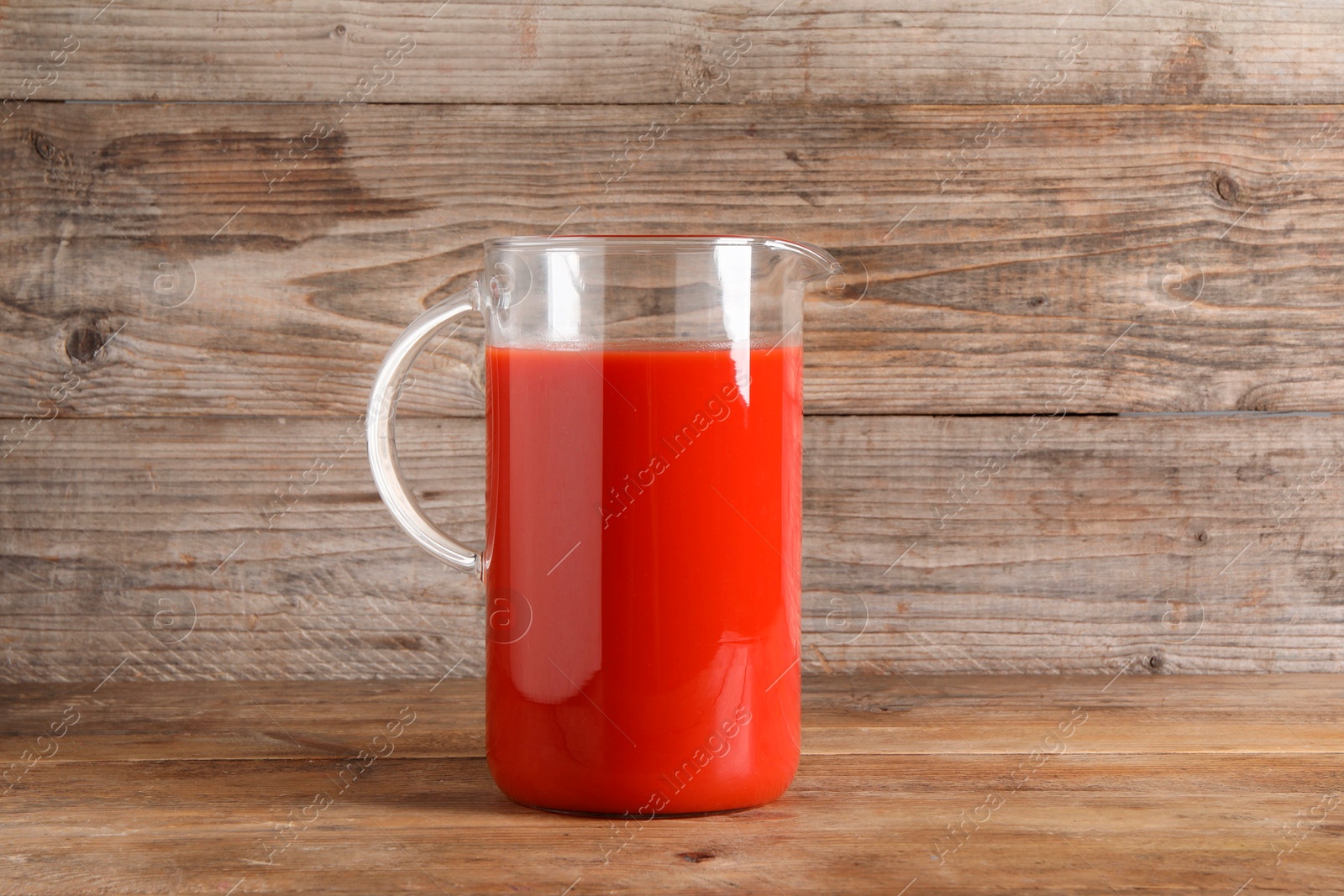 Photo of Fresh tomato juice in glass jug on wooden table