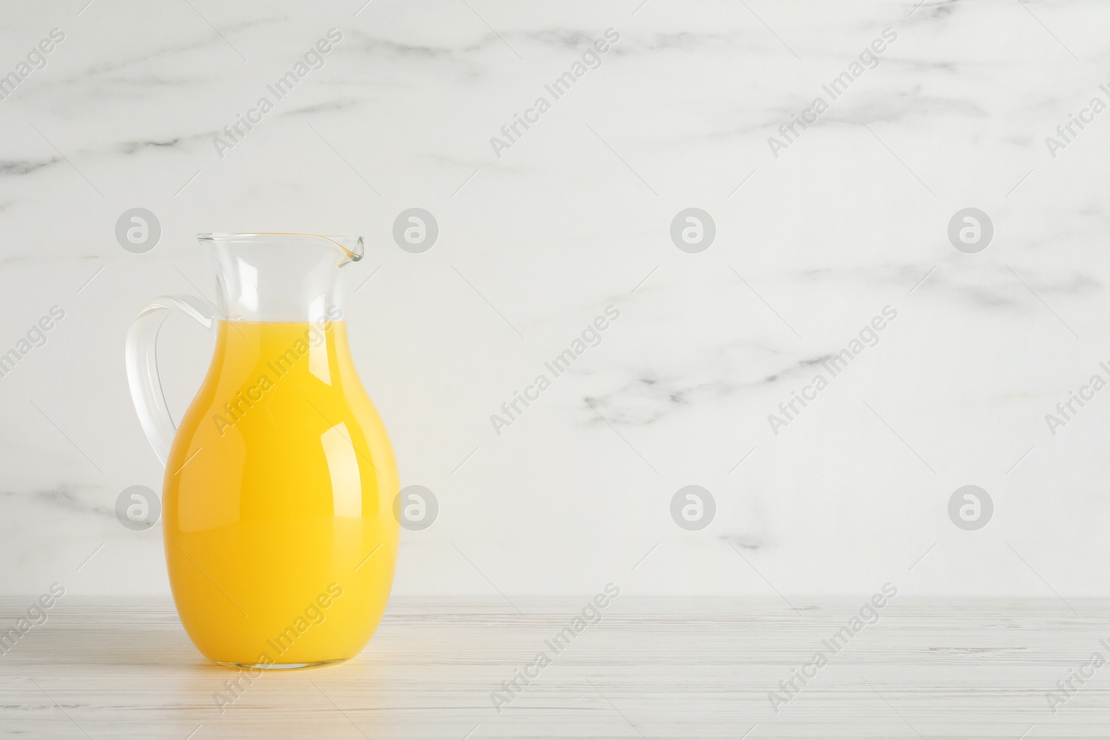 Photo of Fresh orange juice in glass jug on white wooden table, space for text