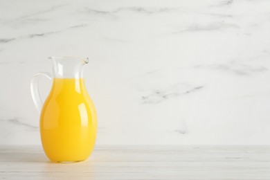 Photo of Fresh orange juice in glass jug on white wooden table, space for text