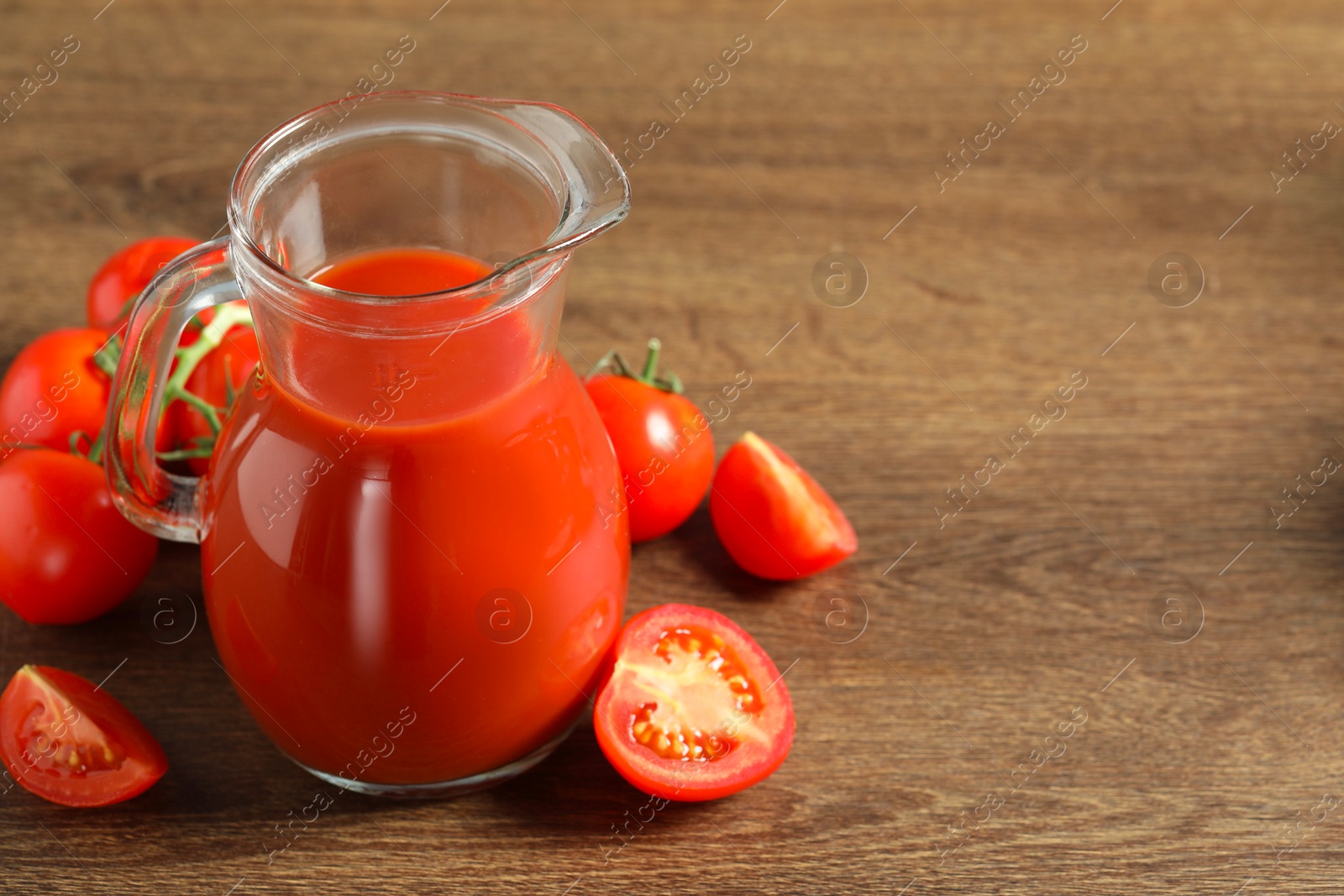 Photo of Tasty tomato juice in jug and vegetables on wooden table. Space for text