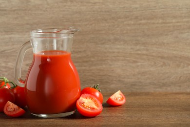 Photo of Tasty tomato juice in jug and vegetables on wooden table. Space for text