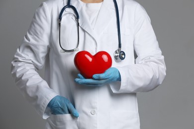 Doctor with red heart on grey background, closeup