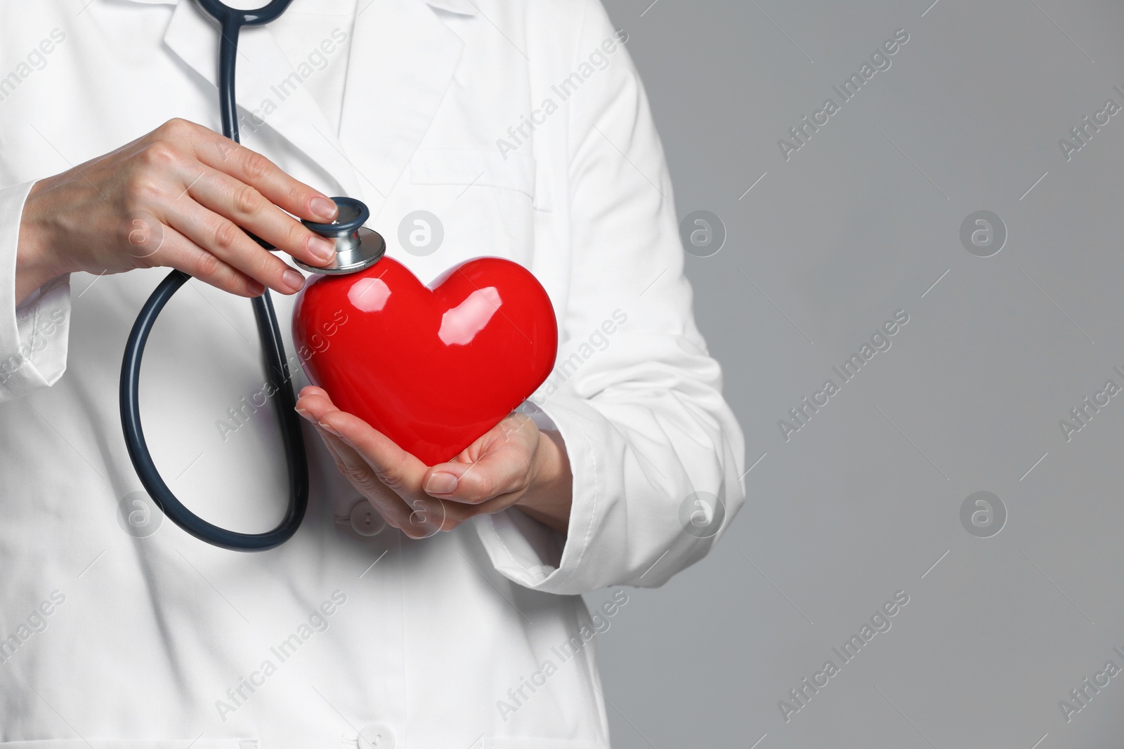 Photo of Doctor with stethoscope and red heart on grey background, closeup. Space for text