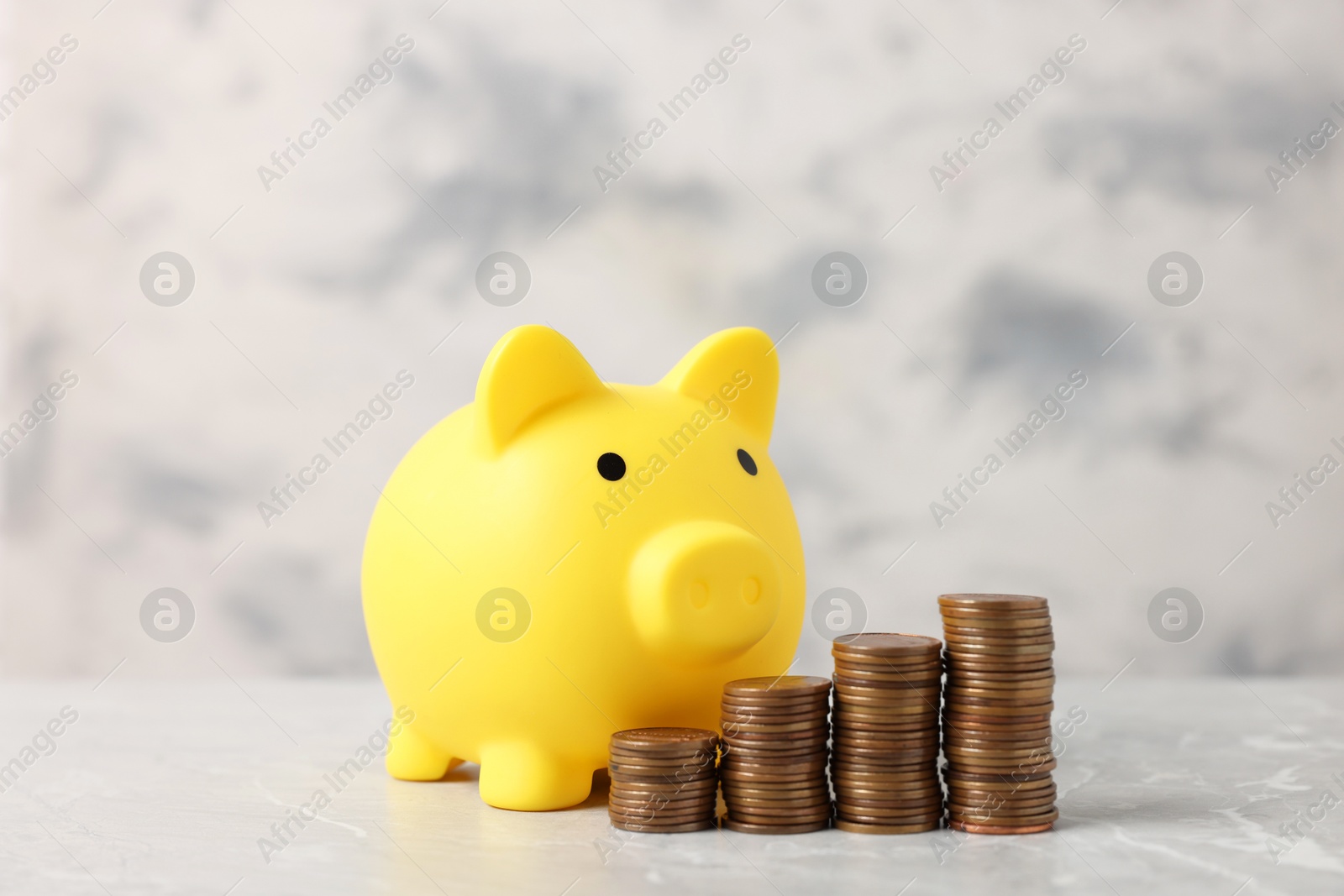 Photo of Yellow piggy bank and stacks of coins on grey marble table