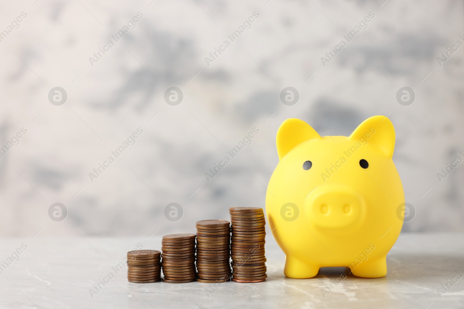 Photo of Yellow piggy bank and stacks of coins on grey marble table