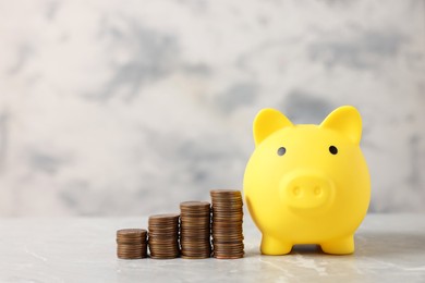 Photo of Yellow piggy bank and stacks of coins on grey marble table