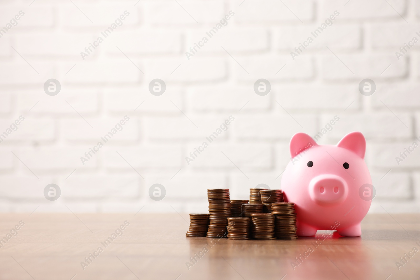 Photo of Pink piggy bank and stacks of coins on wooden table, space for text