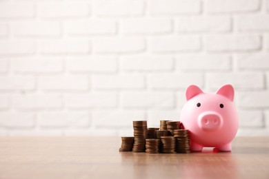 Pink piggy bank and stacks of coins on wooden table, space for text