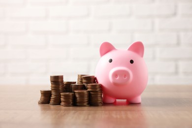 Pink piggy bank and stacks of coins on wooden table