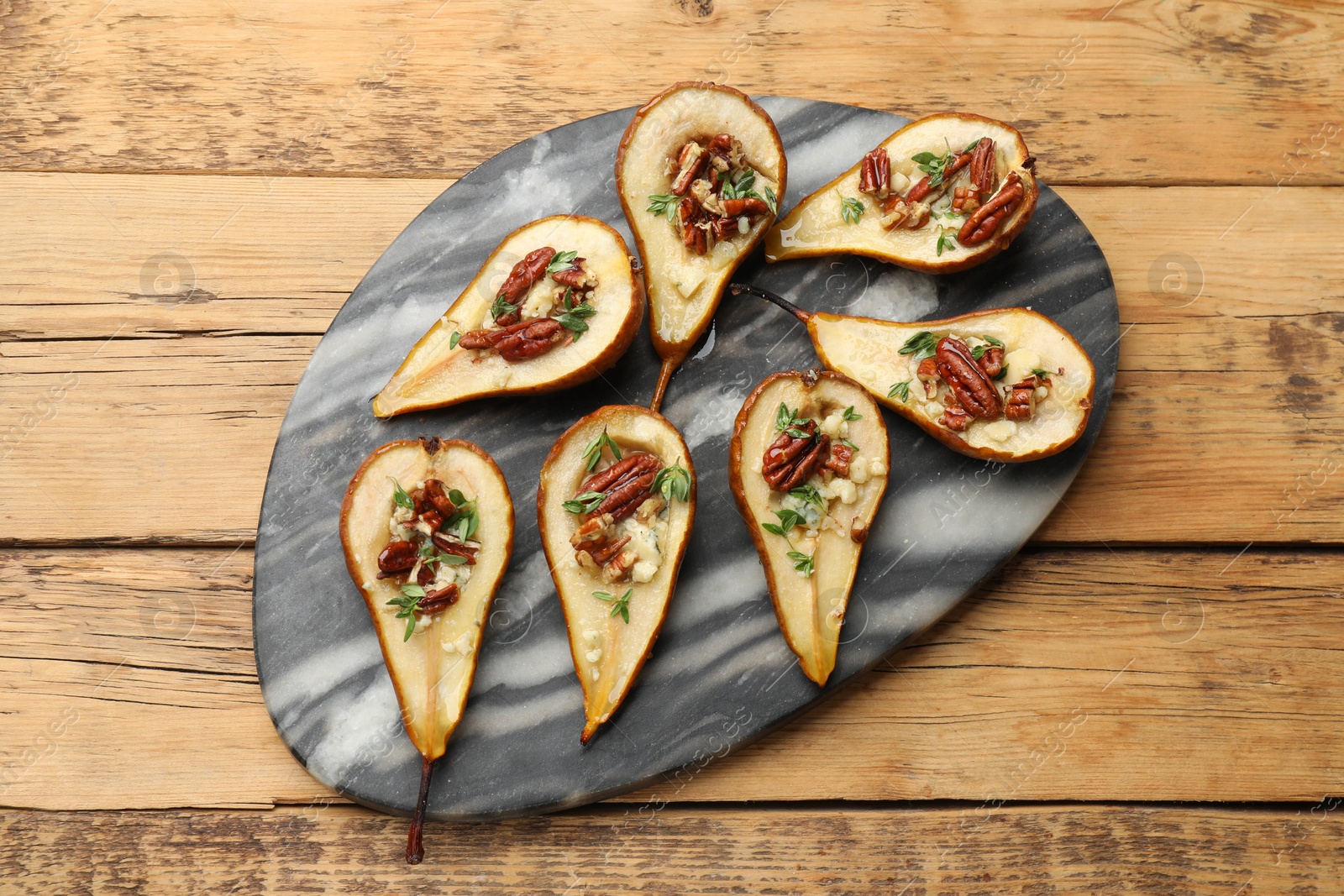 Photo of Tasty baked pears with nuts, blue cheese, thyme and honey on wooden table, top view