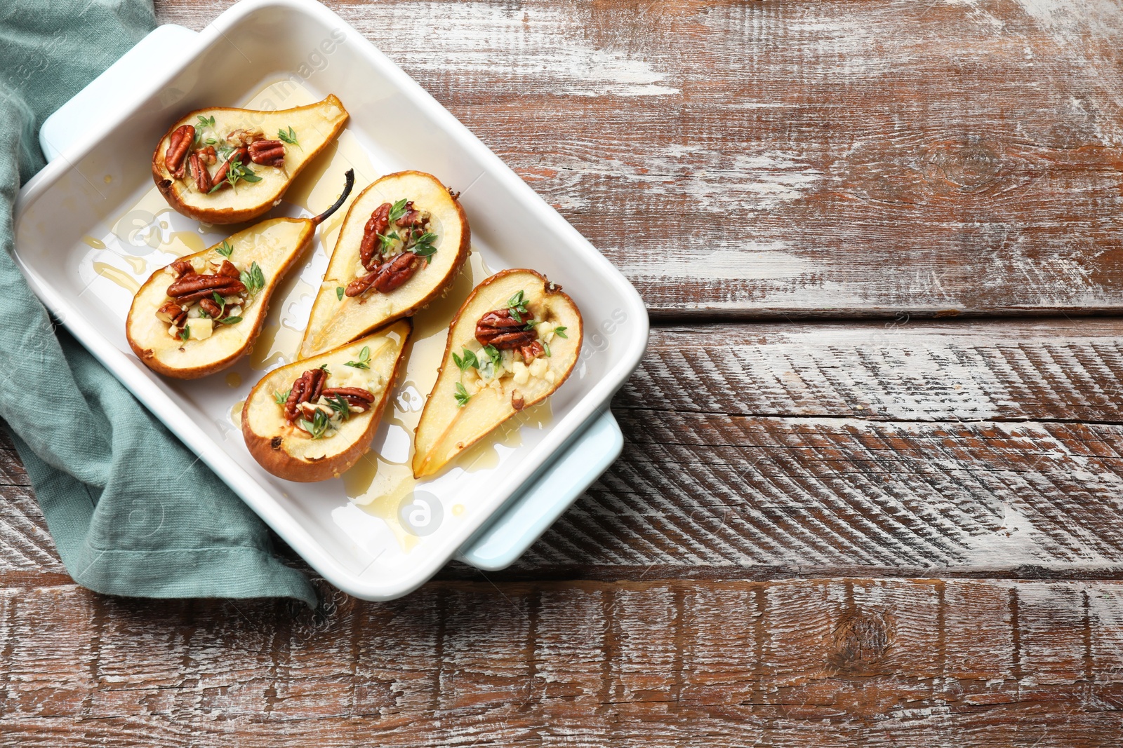 Photo of Tasty baked pears with nuts, blue cheese, thyme and honey in baking dish on wooden table, top view. Space for text