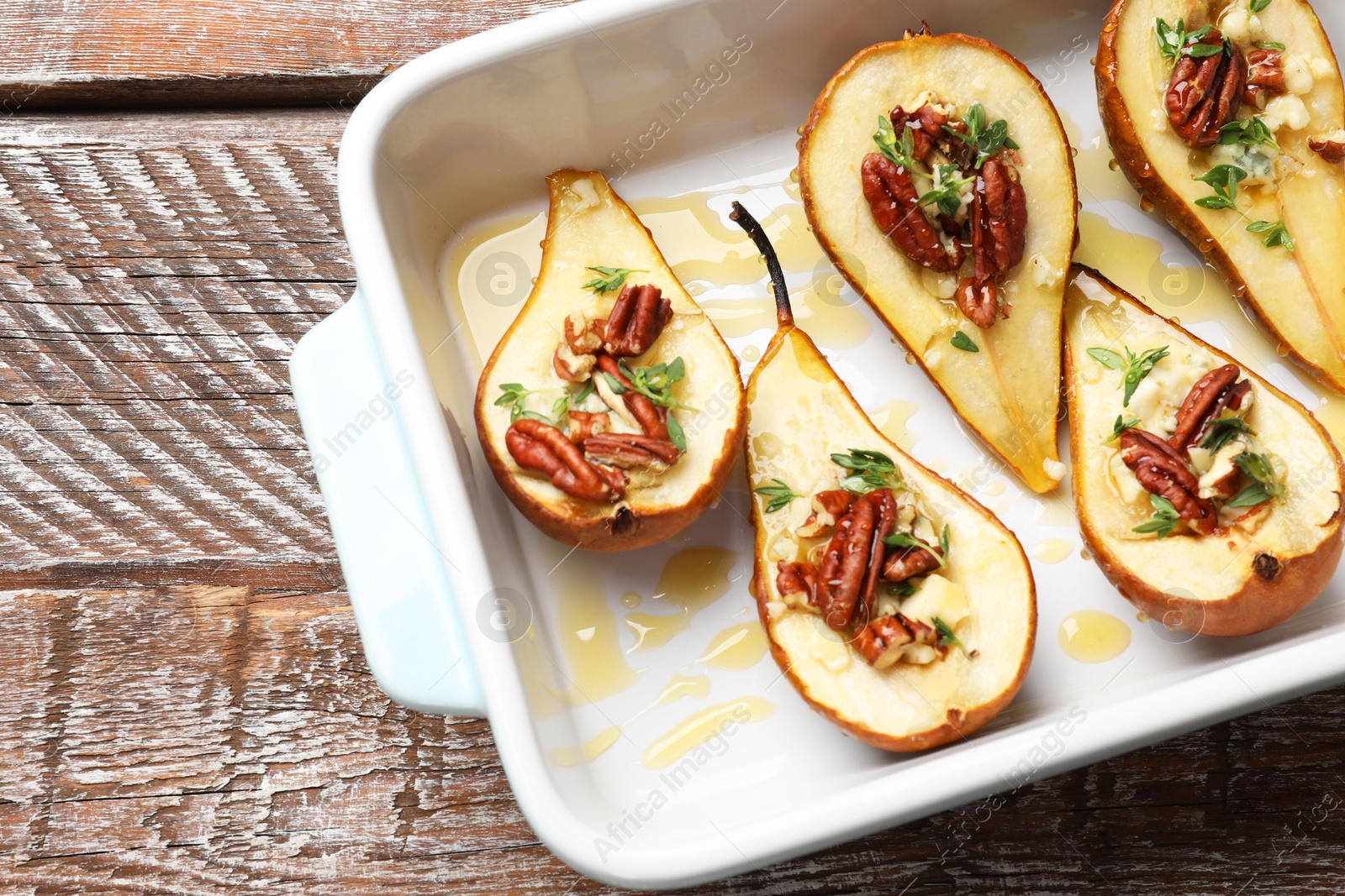 Photo of Tasty baked pears with nuts, blue cheese, thyme and honey in baking dish on wooden table, top view