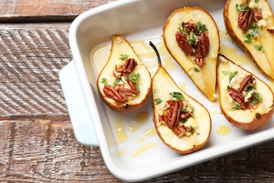 Tasty baked pears with nuts, blue cheese, thyme and honey in baking dish on wooden table, top view