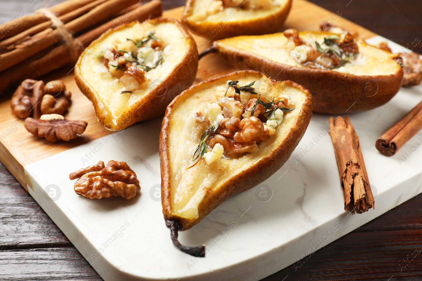 Photo of Tasty baked pears with nuts, blue cheese, thyme, honey and cinnamon sticks on wooden table, closeup