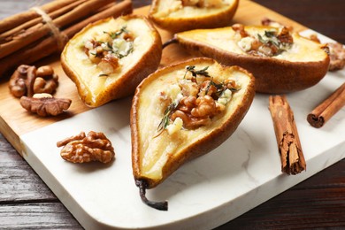 Tasty baked pears with nuts, blue cheese, thyme, honey and cinnamon sticks on wooden table, closeup