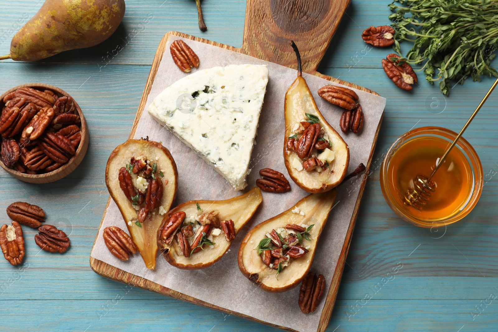 Photo of Delicious baked pears with nuts, blue cheese, thyme and honey on light blue wooden table, flat lay