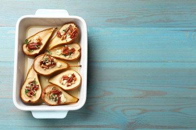 Photo of Delicious baked pears with nuts, blue cheese, thyme and honey in baking dish on light blue wooden table, top view. Space for text