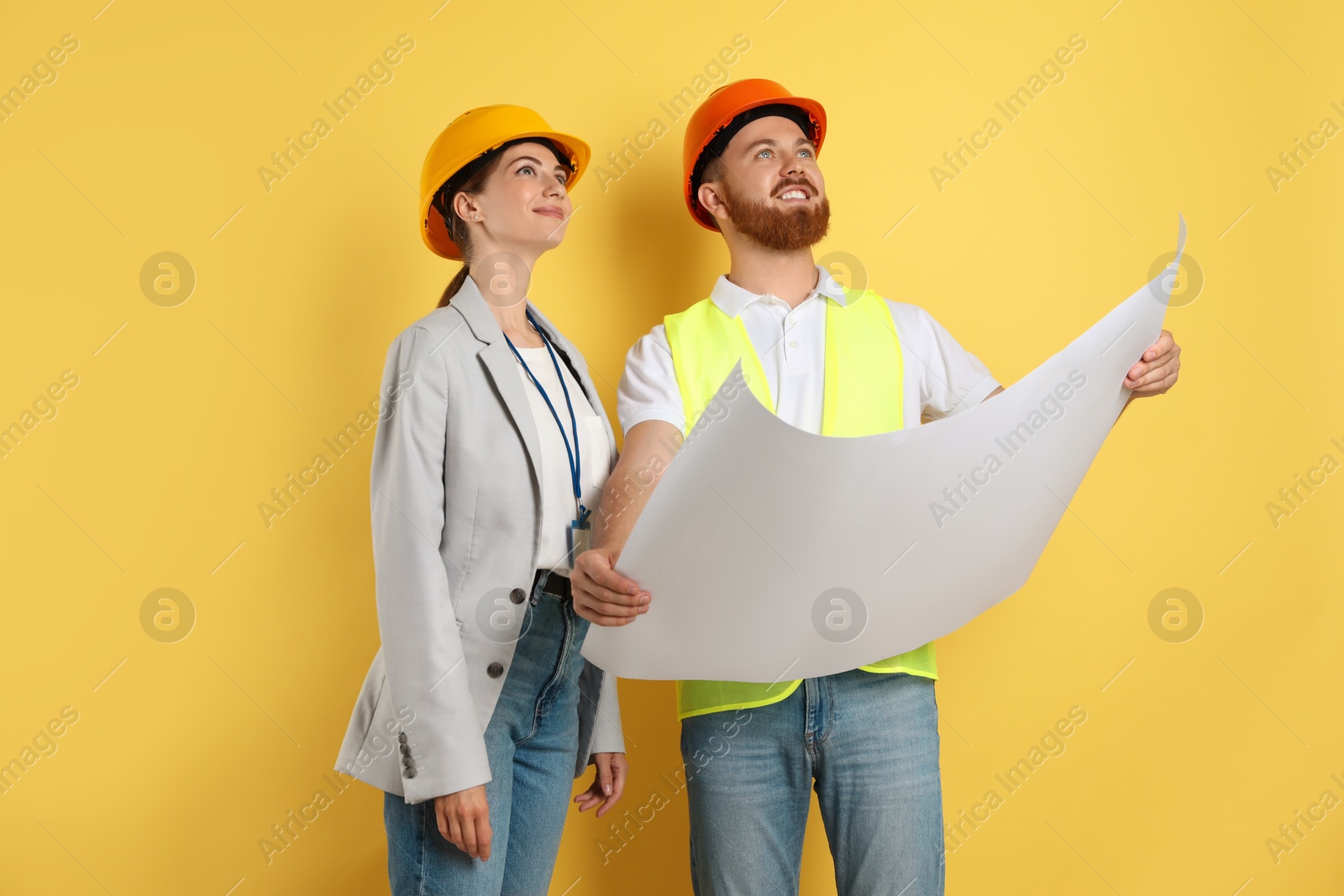 Photo of Engineers in hard hats with draft on yellow background