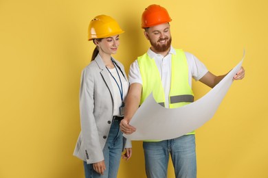 Photo of Engineers in hard hats with draft on yellow background
