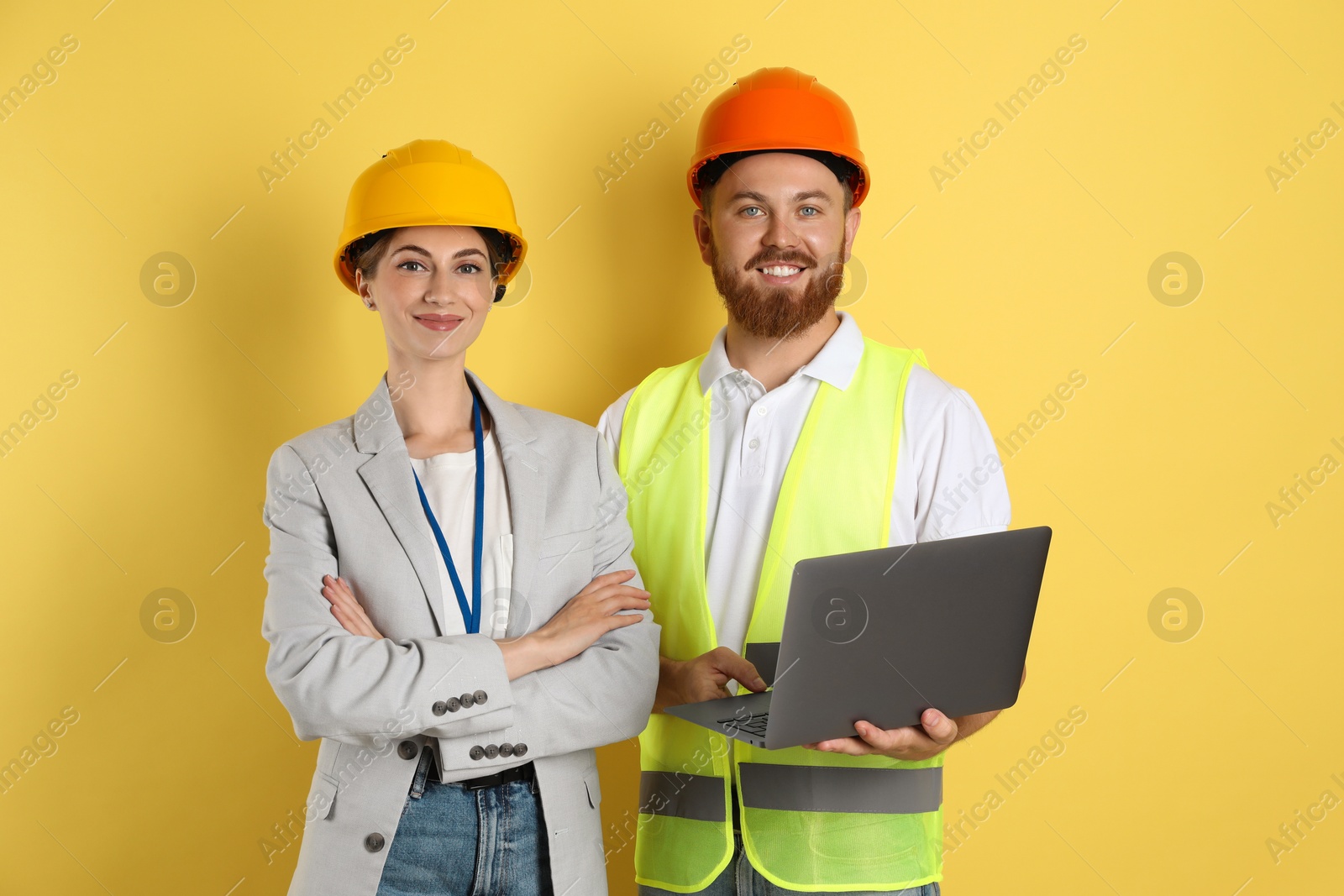 Photo of Engineers in hard hats with laptop on yellow background