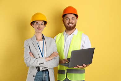 Photo of Engineers in hard hats with laptop on yellow background