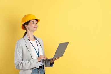 Photo of Engineer in hard hat with laptop on yellow background, space for text