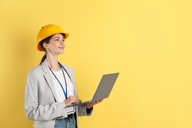 Engineer in hard hat with laptop on yellow background, space for text