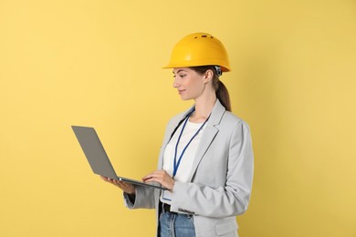 Photo of Engineer in hard hat with laptop on yellow background