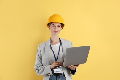 Engineer in hard hat with laptop on yellow background