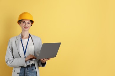 Engineer in hard hat with laptop on yellow background, space for text