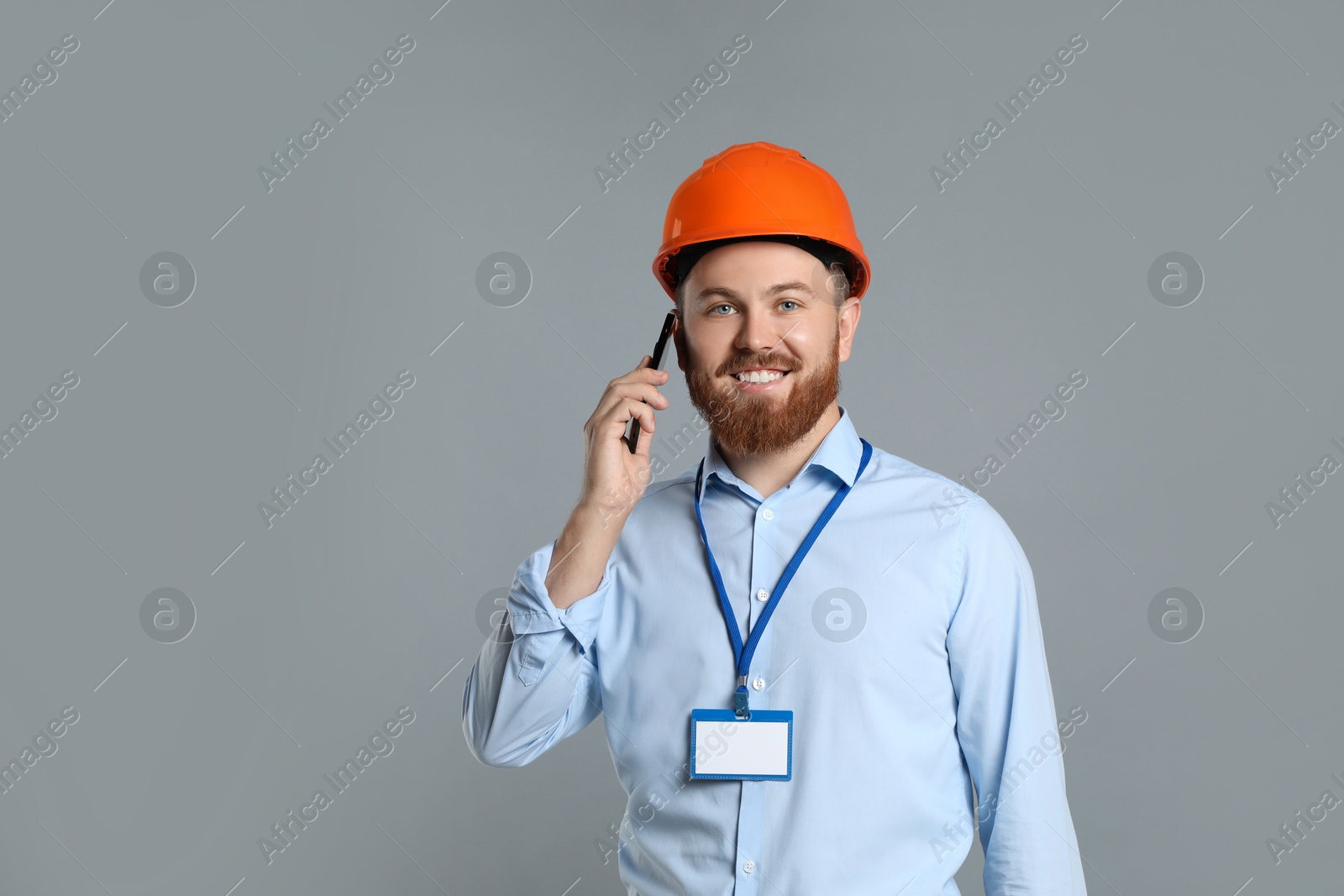 Photo of Engineer in hard hat talking on smartphone against grey background