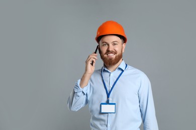 Photo of Engineer in hard hat talking on smartphone against grey background