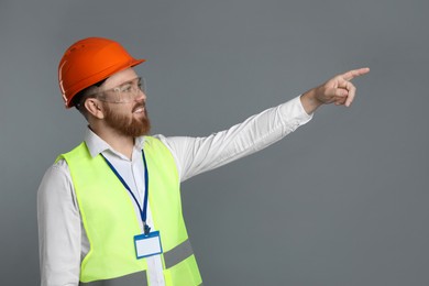 Engineer in hard hat and goggles pointing at something on grey background