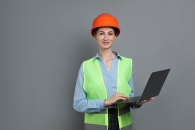 Photo of Engineer in hard hat with laptop on grey background, space for text