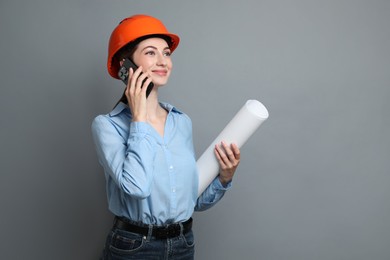 Photo of Engineer in hard hat with draft talking on smartphone against grey background, space for text