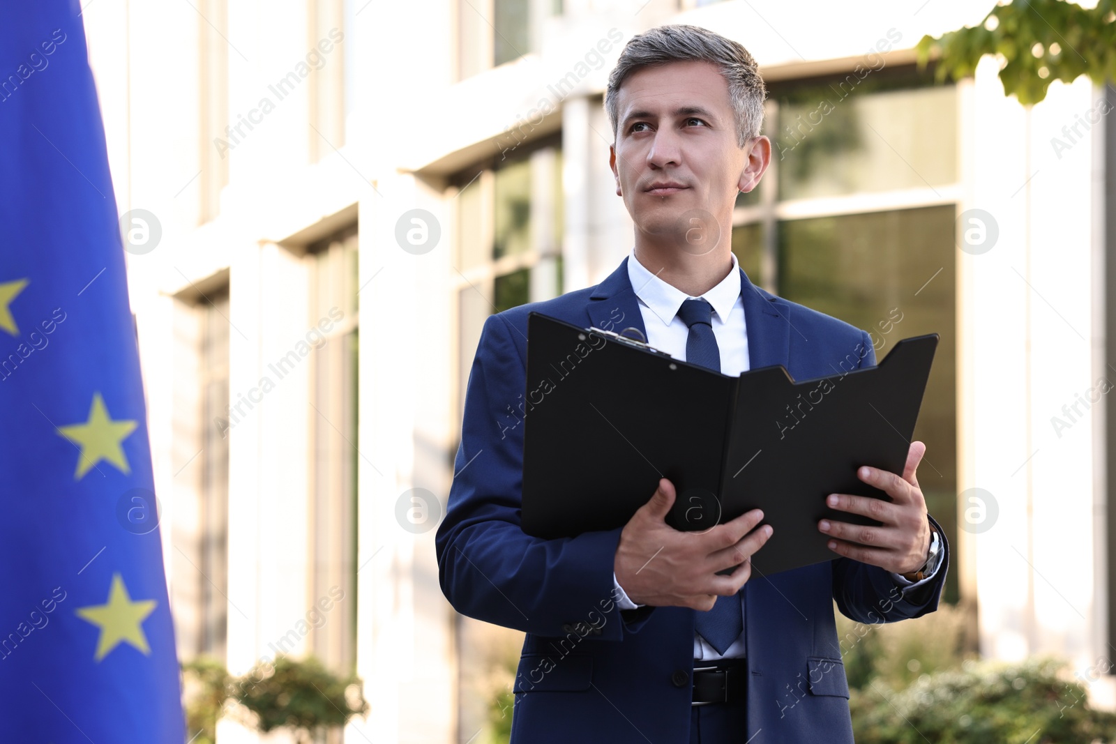 Photo of International relations. Diplomat with clipboard near flag of European Union outdoors