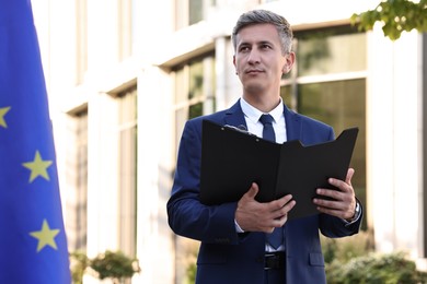 International relations. Diplomat with clipboard near flag of European Union outdoors