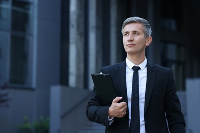 Photo of International relations. Diplomat with clipboard in suit outdoors, space for text