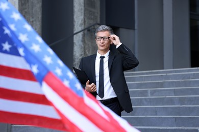 International relations. Diplomat with clipboard near flag of USA outdoors