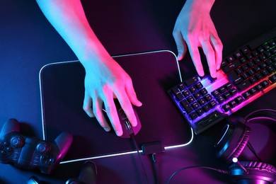 Photo of Gamer using modern wired computer mouse at dark table in neon lights, top view