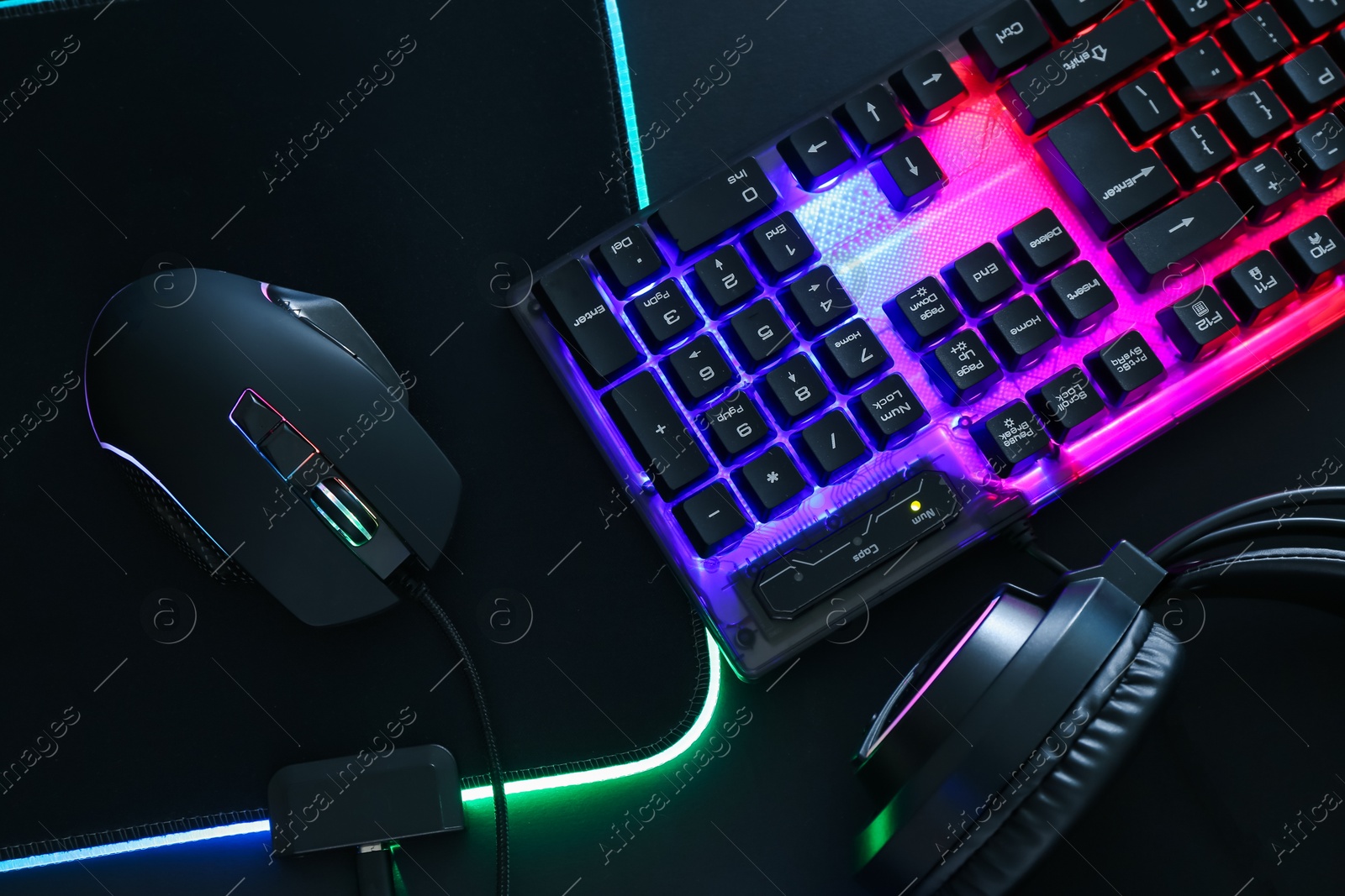 Photo of Computer mouse, RGB keyboard and headset on black background, flat lay