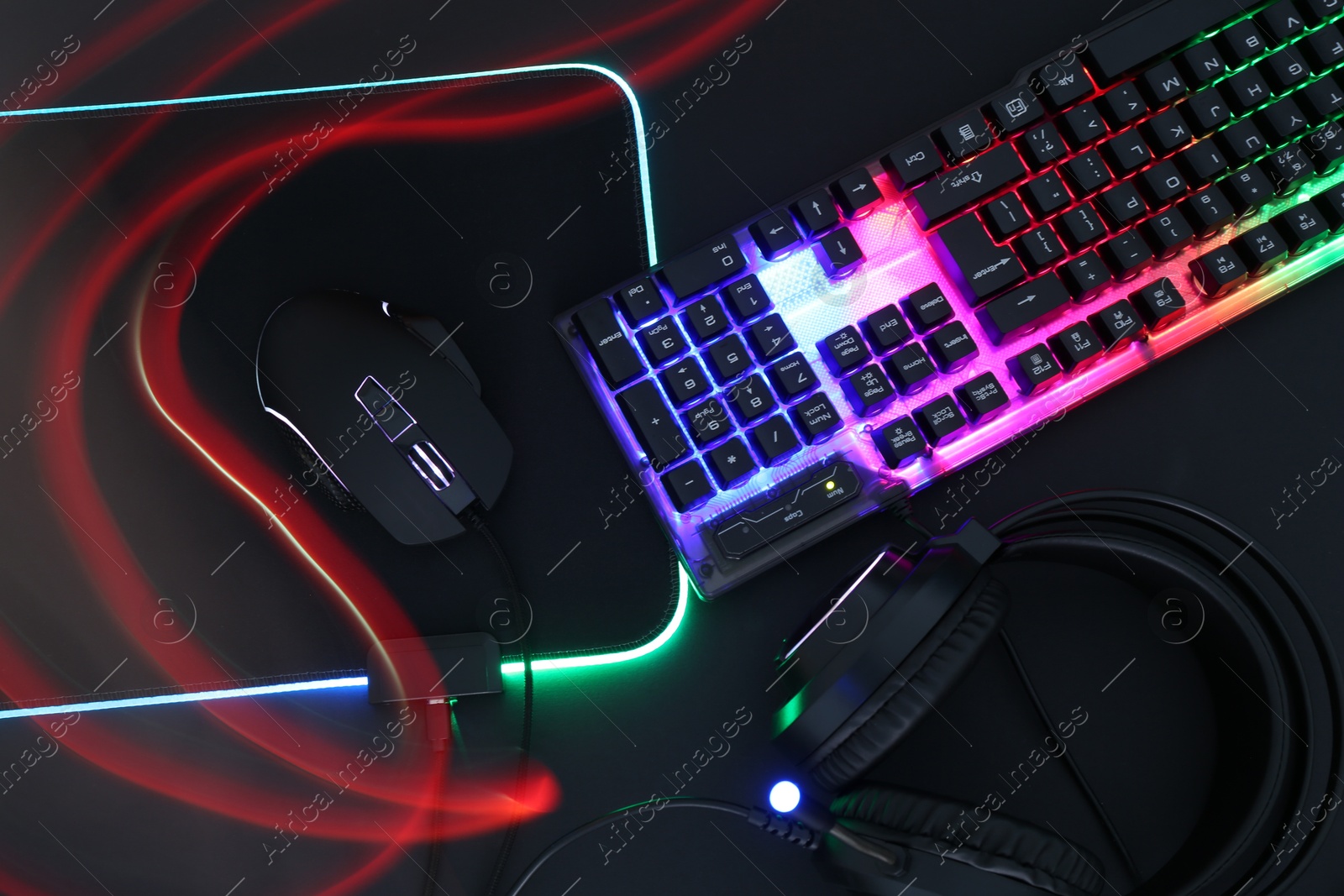 Photo of Computer mouse, RGB keyboard and headset in neon lights on black background, flat lay