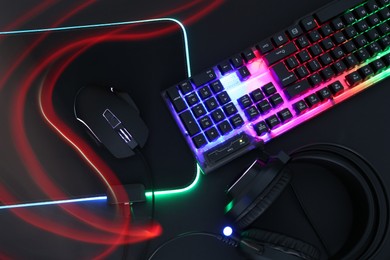 Photo of Computer mouse, RGB keyboard and headset in neon lights on black background, flat lay