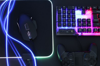 Photo of Computer mouse, RGB keyboard and game controller in neon lights on black background, flat lay